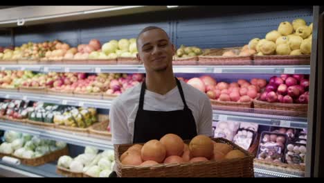 Young-man-in-apron-hold-basket-with-oranges-and-pose-on-camera
