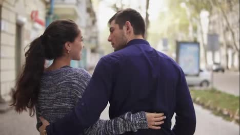 Close-up-back-view-of-young-beautiful-couple-walking-in-the-street-embracing-each-other-and-talking.-Romantic-date