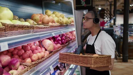 Man-worker-in-black-apron-and-gloves-stocking-the-fruits-in-supermarket-while-listen-to-the-music