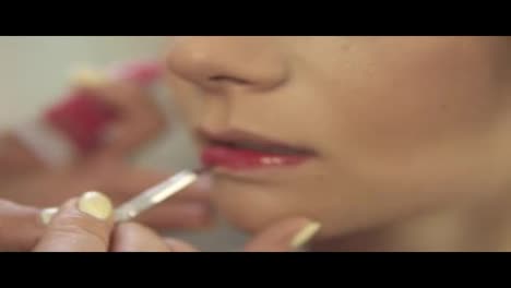 Make-up-artist-applying-red-lipstick-using-a-brush.-Close-Up-view.-Slow-Motion-shot