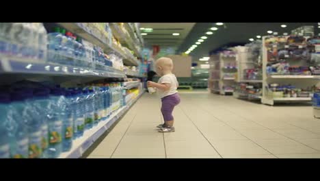 Cute-little-child-walking-in-water-department-in-the-supermarket-and-choosing-bottles-inside-of-a-big-marketplace,-carefully