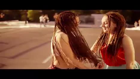 Two-happy-women-with-dreads-walking-on-the-empty-road-and-talking-in-summer.-Two-hipster-girls-laughing-and-dancing-during-a