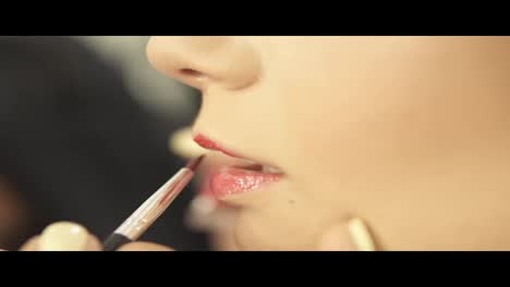 Makeup-artist-paints-lips-of-a-beautiful-girl-using-lipstick-brush.-Model-with-lipstick.-Pink-Lipstick-on-lips.-Trendy-shades-of