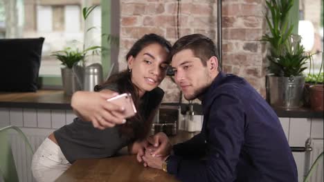 Attractive-young-couple-taking-selfie-at-restaurant,-cafe.-Happy-couple-during-holidays-taking-selfie-while-sitting-at-the-table