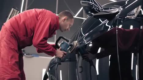 Man-in-red-work-suit-polishing-black-car-at-auto-center