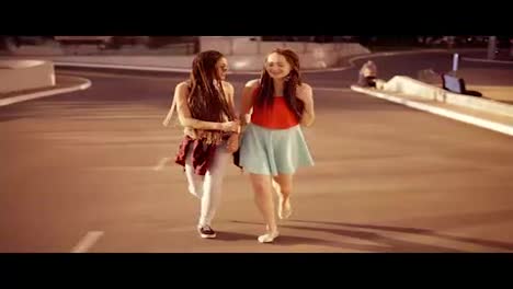 Two-happy-women-with-dreads-walking-on-the-empty-road-and-talking-in-summer.-Two-hipster-girls-laughing-and-hugging-each-other