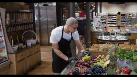 Worker-in-black-apron-arranging-fresh-fruits-in-supermarket-section
