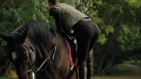 Female-equestrian-climbs-on-horseback-with-help-of-stirrup-and-strokes-a-beautiful-brown-horse