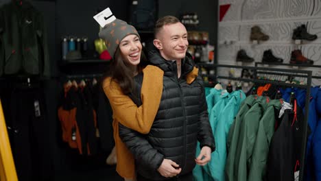 Young-man-trying-at-winter-jacket-in-clothing-store-with-his-girlfriend