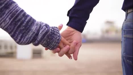Close-Up-view-of-a-young-couple-on-the-beach-holding-hands-and-walking-together.-Slow-Motion-shot