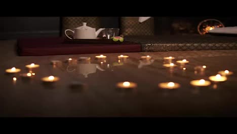 Fiery-heart.-Candles-arranged-in-a-heart-shape.-Glowing-candles-in-a-heart-shape-with-a-teapot-on-the-background.-Slow-Motion-shot