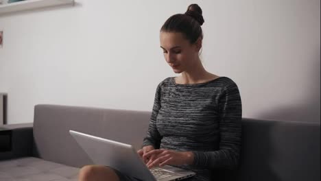 Mujer-Concentrada-Trabajando-En-Casa:-Está-Sentada-En-El-Sofá,-Trabajando-Con-Una-Computadora-Portátil-Y-Escribiendo-Texto-Mirando-La-Pantalla