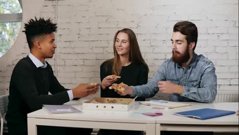 Business-team-of-young-people-enjoying-pizza-together-in-the-office,-millennials-group-talking-having-fun-sharing-lunch-in-cozy