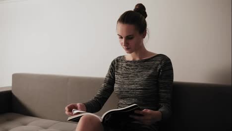 Portrait-of-a-young-attractive-woman-reading-a-magazine-while-sitting-on-the-couch-in-her-living-room.-Leisure-time