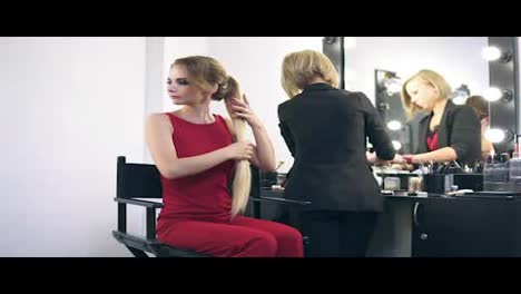 Make-up-artist-using-big-brush-to-apply-face-powder-and-finishing-make-up-for-a-young-blonde-woman-in-red-dress.-Beauty-salon