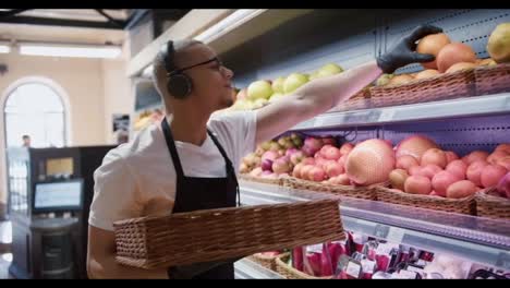 Hombre-Trabajador-Almacenando-Las-Frutas-En-El-Supermercado-Mientras-Escucha-La-Música,-Vista-Lateral