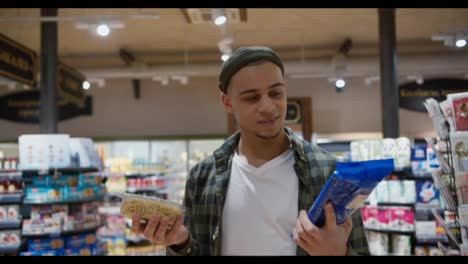 A-guy-chooses-products-in-the-grocery-store,-thinking-between-cooked-and-raw-pasta