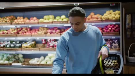 Young-attractive-mixed-race-man-choosing-grapes-in-the-supermarket,-putting-to-the-basket
