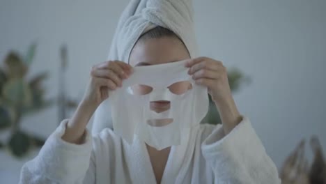 Porträt-Einer-Jungen-Hausfrau,-Die-Im-Badezimmer-Eine-Gewebe-Gesichtsmaske-Zur-Hautpflege-Aufträgt