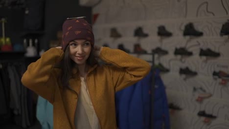 Smiling-woman-trying-on-a-new-colorful-winter-hat-in-a-store