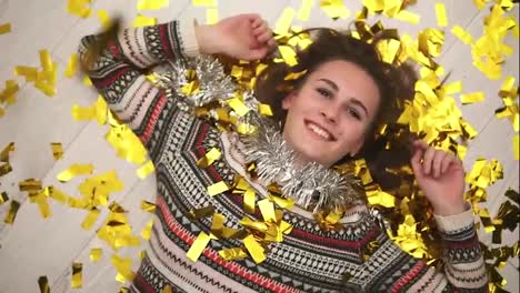 Round-camera-movement:-Happy-smiling-girl-lying-on-the-floor,-the-golden-confetti-falling-on-her.-Slow-motion-shot