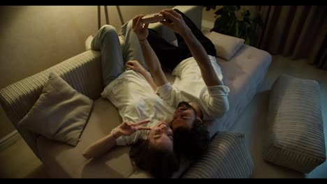 Cheerful-beautiful-young-couple-selfie-on-sofa-home-using-polaroid-camera