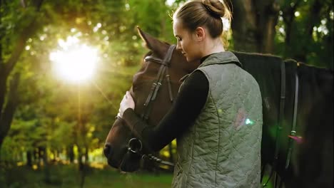 Close-Up-view-of-young-beautiful-woman-petting-brown-horse-while-standing-in-the-forest-on-a-sunny-day.-Lens-flare
