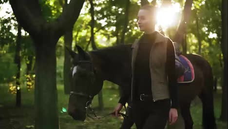 Slow-Motion-shot-of-attractive-young-female-jockey-walking-with-brown-horse-with-white-spot-on-forehead-in-the-forest-during-sunny