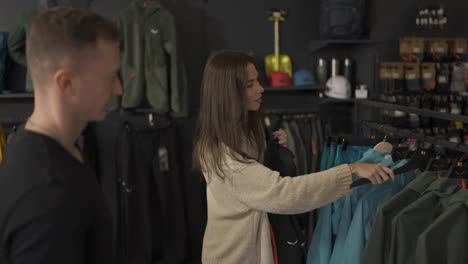 Lovely-couple-shopping-in-mall-choosing-sportswear,-a-girl-trying-coat