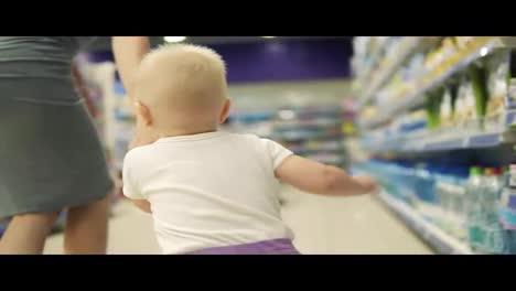 Young-attractive-mother-in-shopping-together-with-her-cute-baby-in-the-supermarket-together,-holding-hands,-walking-to-their