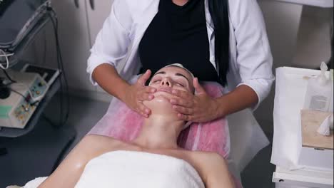 Concentrated-female-cosmetologist-is-making-face-massage-in-spa-salon.-Young-woman-with-her-eyes-closed-is-lying-on-the-couch