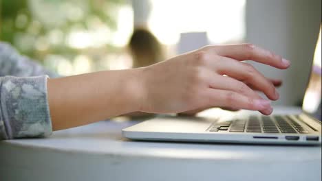 Close-Up-view-of-female-hands-working-on-laptop-computer.-Woman-is-sitting-near-the-window-in-cafe-and-typing.-White-cup-with