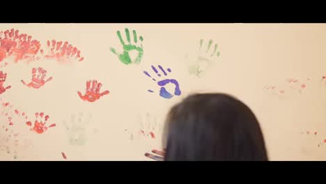 Happy-cute-little-boy-and-his-young-mother-are-having-fun-leaving-their-colorful-handprints-on-the-wall.-Young-happy-family