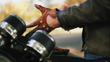 Side-view-of-and-unrecognizable-motorcyclist-taking-brown-leather-gloves-and-wearing-special-leather-mitts-for-riding-in-slow