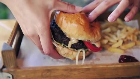 Female-hands-taking-big-tasty-burger-from-a-wooden-tray-and-getting-ready-to-eat-it.-Slow-Motion-shot