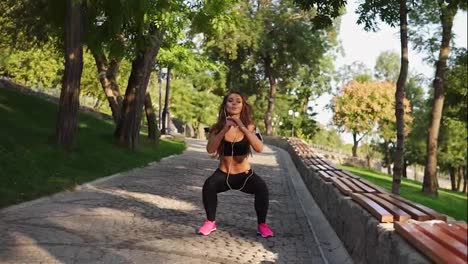 Young-woman-exercising,-doing-squats-in-the-park-listening-to-the-music.-Morning-sport.-Slow-Motion-shot