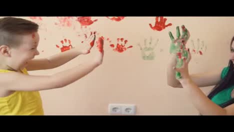 Young-mother-with-her-little-boy-are-mixing-colors-at-their-hands-yo-leave-beautiful-handprints-on-the-wall.-Mother-and-child