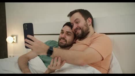 Una-Pareja-Gay-Se-Hace-Selfie,-Se-Toma-Una-Foto-En-La-Cama-Y-Se-Divierte-Juntos-En-El-Dormitorio-Por-La-Mañana