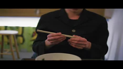 Close-Up-view-of-man's-hands-taking-chopsticks-and-starting-to-eat-noodles.-Noodles-with-vegetables.-Dinner-in-japanese