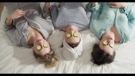 Happy-friends-with-cucumber-mask-relaxing-on-the-bed-with-towels-on-head