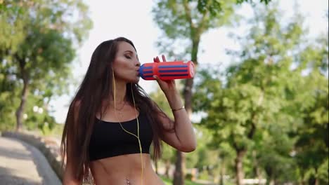 Young-fitness-woman-drinking-water-from-plastic-bottle-after-morning-jogging,-listening-to-the-music-and-drinking-water-from-the