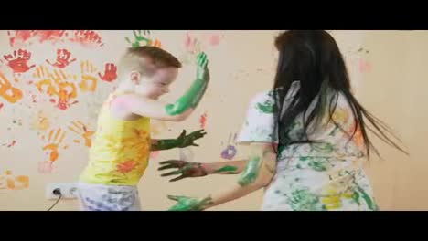 Young-mother-with-her-little-boy-are-mixing-colors-at-their-hands-yo-leave-beautiful-handprints-on-the-wall.-Their-clothes-are