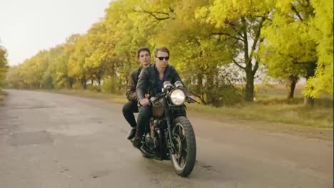 Tracking-shot-of-handsome-man-in-sunglasses-riding-a-motorcycle-with-his-girlfriend-behind,-traveling-together-on-the-asphalt