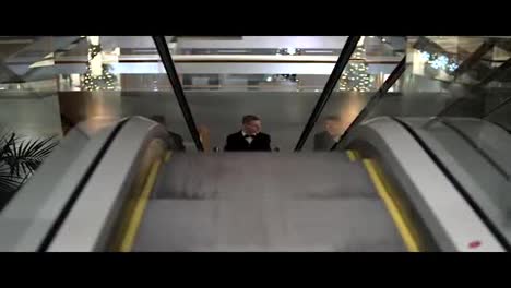 Ein-Junger-Mann-In-Einem-Schwarzen-Anzug-Mit-Fliege-Kommt-In-Einem-Einkaufszentrum-Auf-Die-Rolltreppe