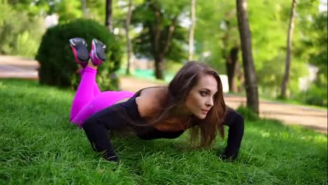 Attractive-brunette-woman-doing-push-up-workout-exercise-on-the-grass-in-the-park.-Push-ups-with-knees.-Slow-Motion-shot