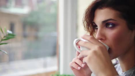 Beautiful-young-woman-dreaming-with-cup-of-hot-coffee-over-window.-Close-Up-view.-Slow-Motion-shot
