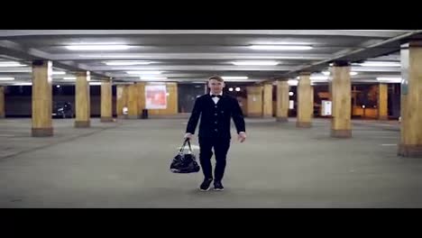 Young-businessman-in-a-black-suit-with-bow-tie-walking-on-the-parking-with-big-leather-bag.-Slow-Motion