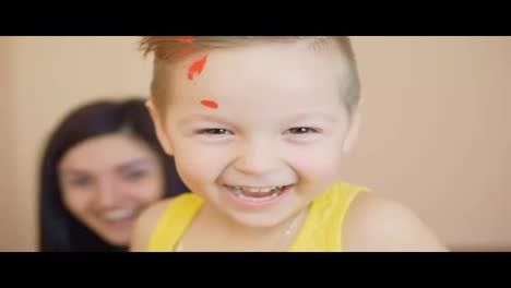 Happy-cute-little-boy-is-having-fun-leaving-his-red-handprints-on-the-wall.-Close-Up-view-of-the-smiling-happy-child.-Mother-and