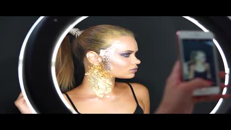 View-in-the-mirror-of-a-beautiful-long-haired-model-with-stylish-golden-makeup-and-covered-in-golden-metallic-pieces-making