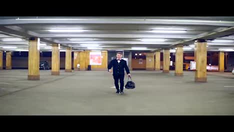 Young-blonde-businessman-in-a-black-suit-with-bow-tie-walking-on-the-parking-with-big-leather-bag.-Slow-Motion